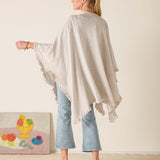 Woman wearing a beige poncho over a light blue outfit, standing against a plain background.
