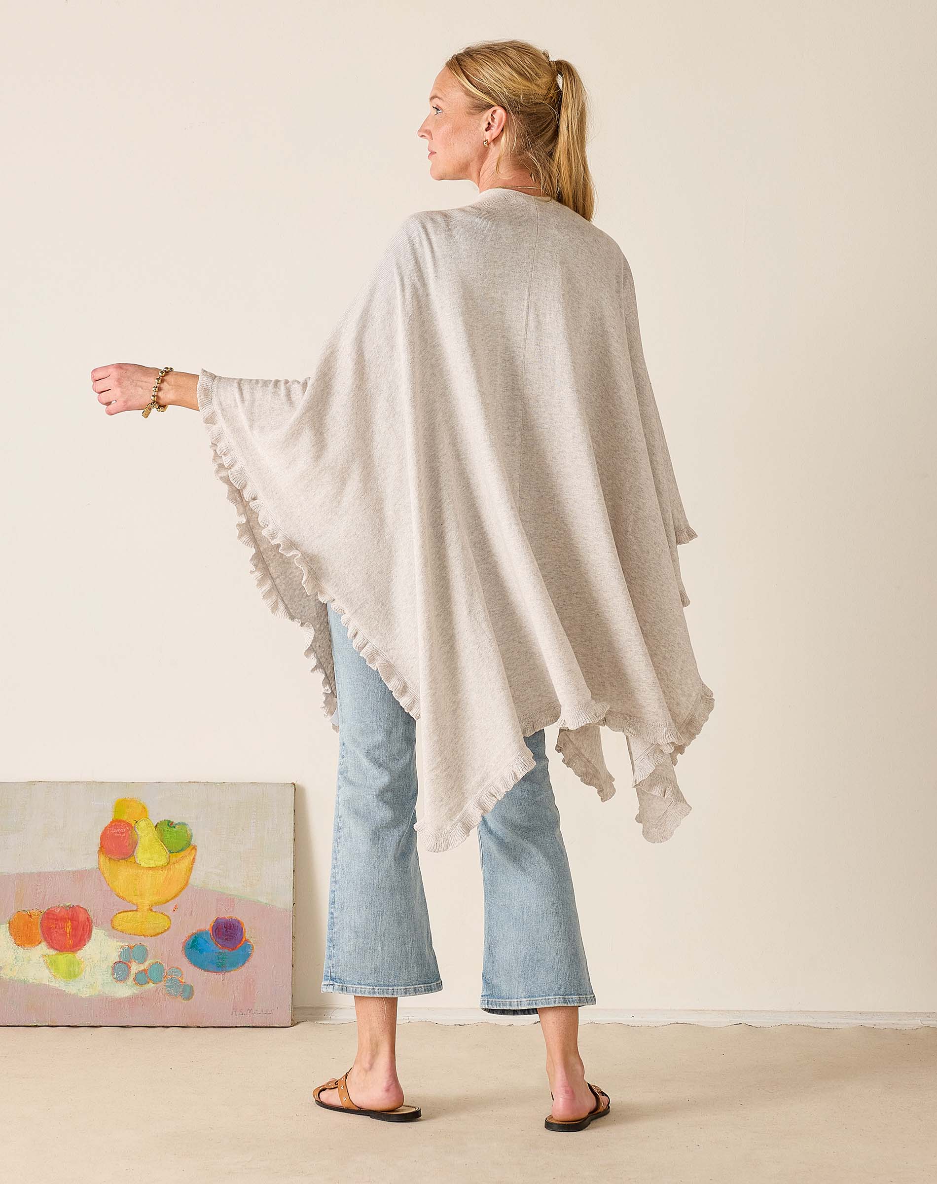 Woman wearing a beige poncho over a light blue outfit, standing against a plain background.