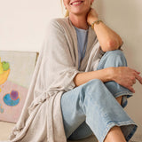 Woman sitting on a couch wearing a light gray cardigan and blue jeans, smiling.