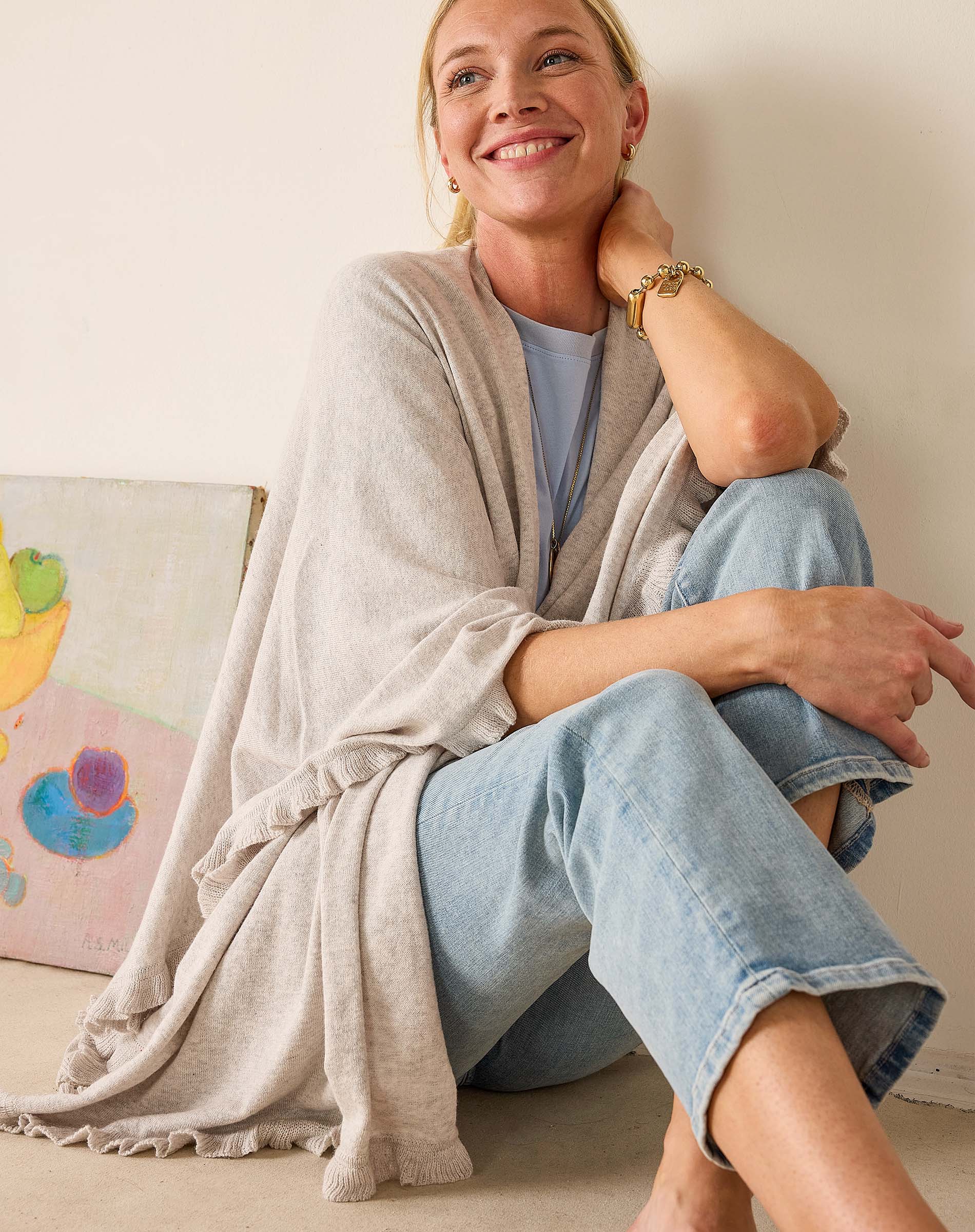 Woman sitting on a couch wearing a light gray cardigan and blue jeans, smiling.