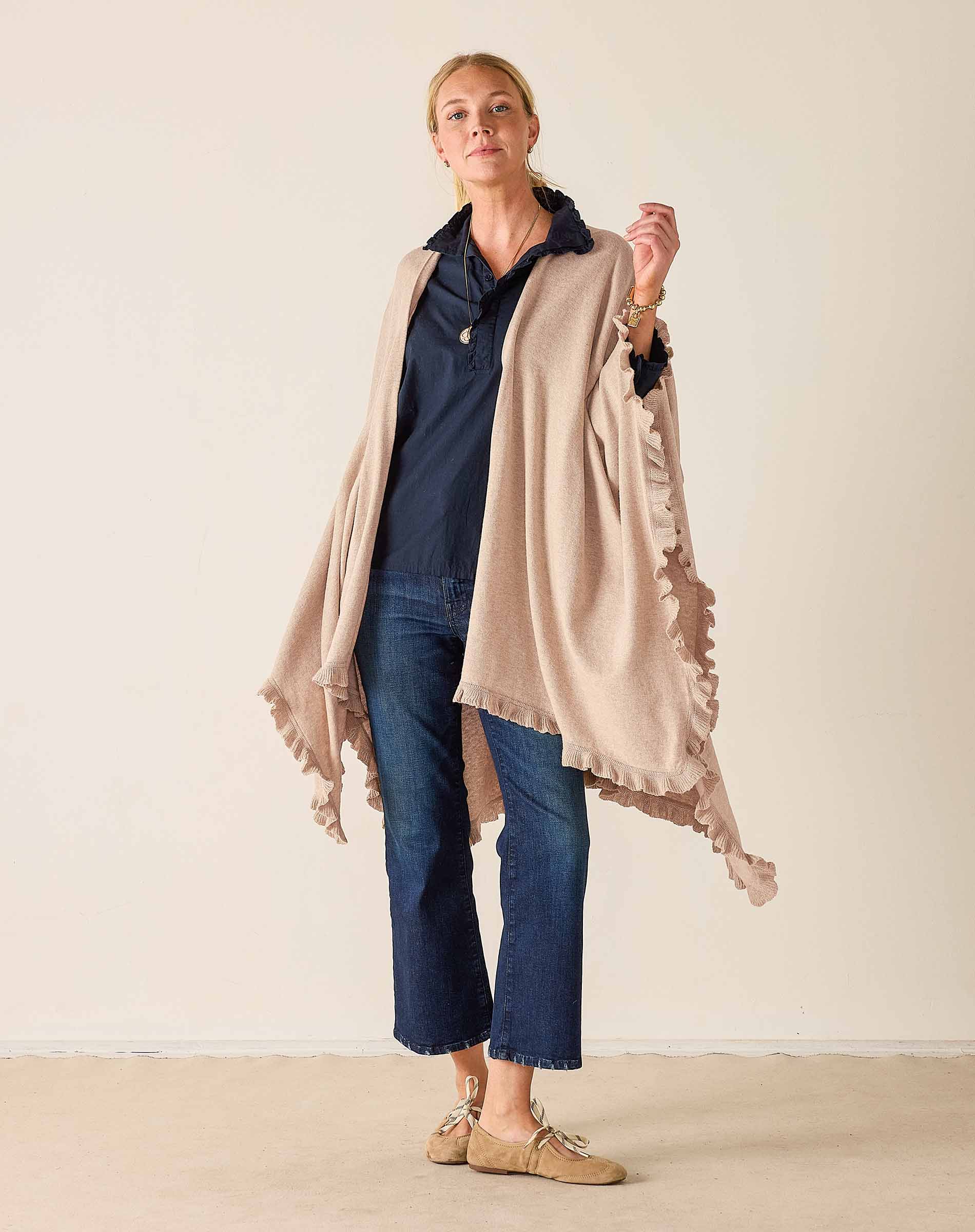 Woman wearing a beige scarf, navy shirt, and blue jeans against a plain background