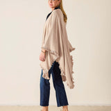 Woman wearing a beige poncho and blue jeans against a plain background