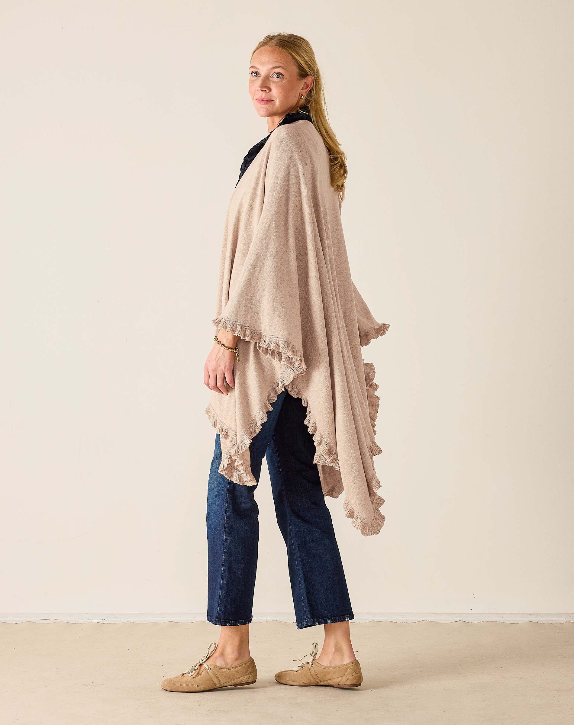 Woman wearing a beige poncho and blue jeans against a plain background