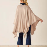 Woman wearing a beige poncho over a navy outfit against a plain background