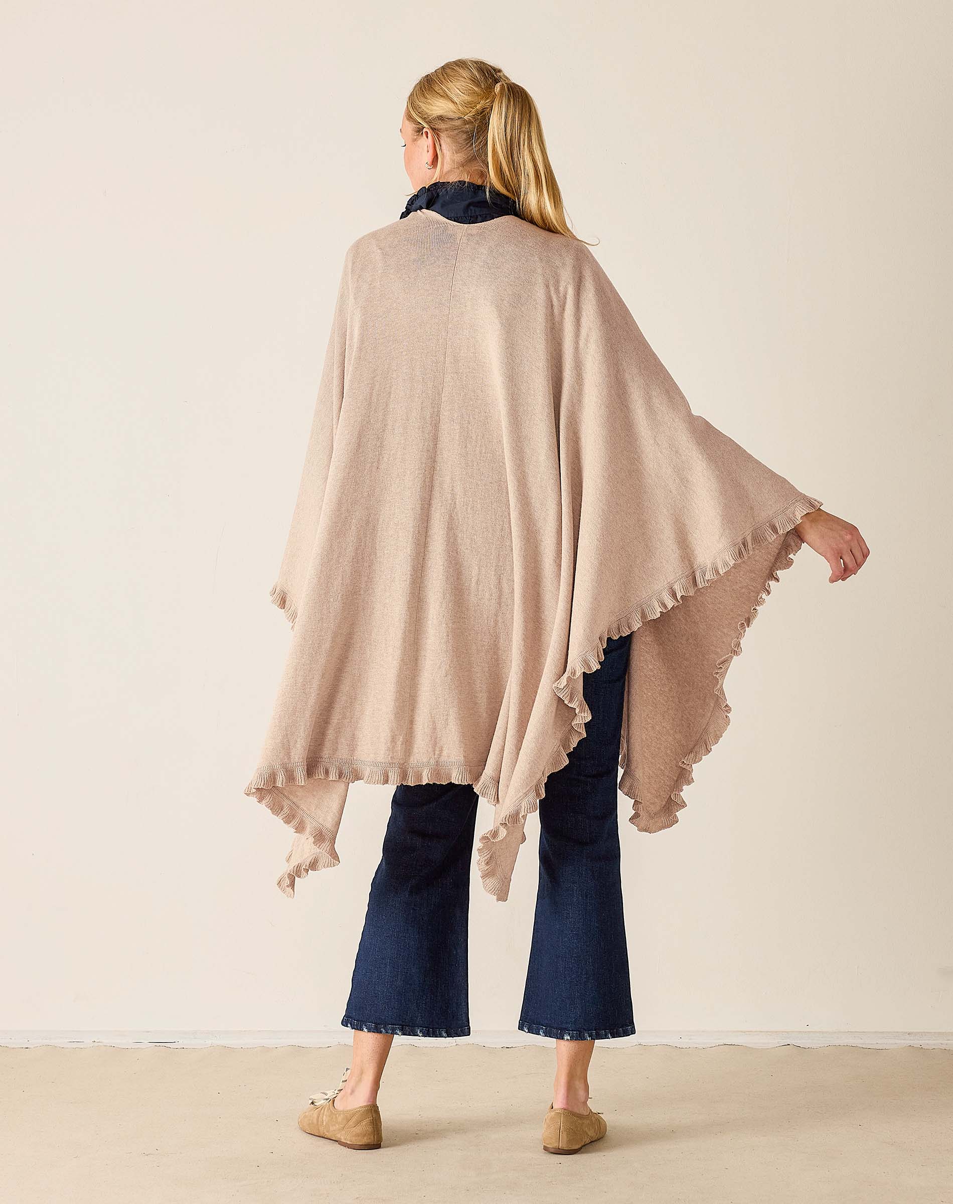 Woman wearing a beige poncho over a navy outfit against a plain background