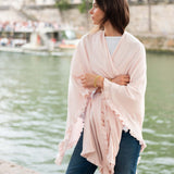 Woman wearing a light pink scarf by a waterfront with a blurred background