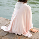 Person wearing a light pink dress sitting by a body of water.