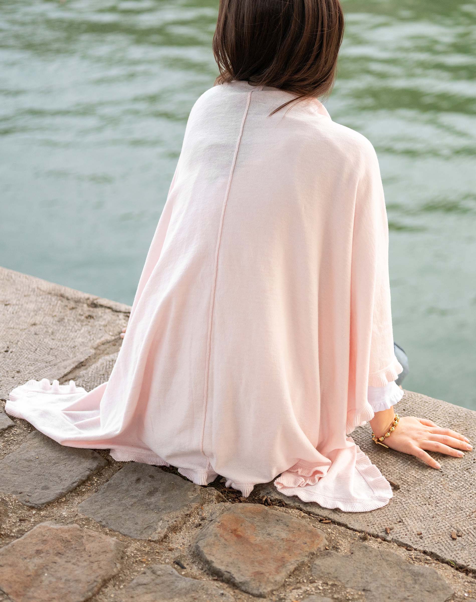 Person wearing a light pink dress sitting by a body of water.