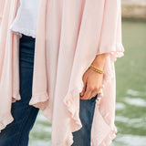 Person wearing a light pink cardigan over a white shirt with a blurred natural background