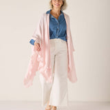 Woman wearing a blue shirt, white pants, and a pink cardigan against a white background