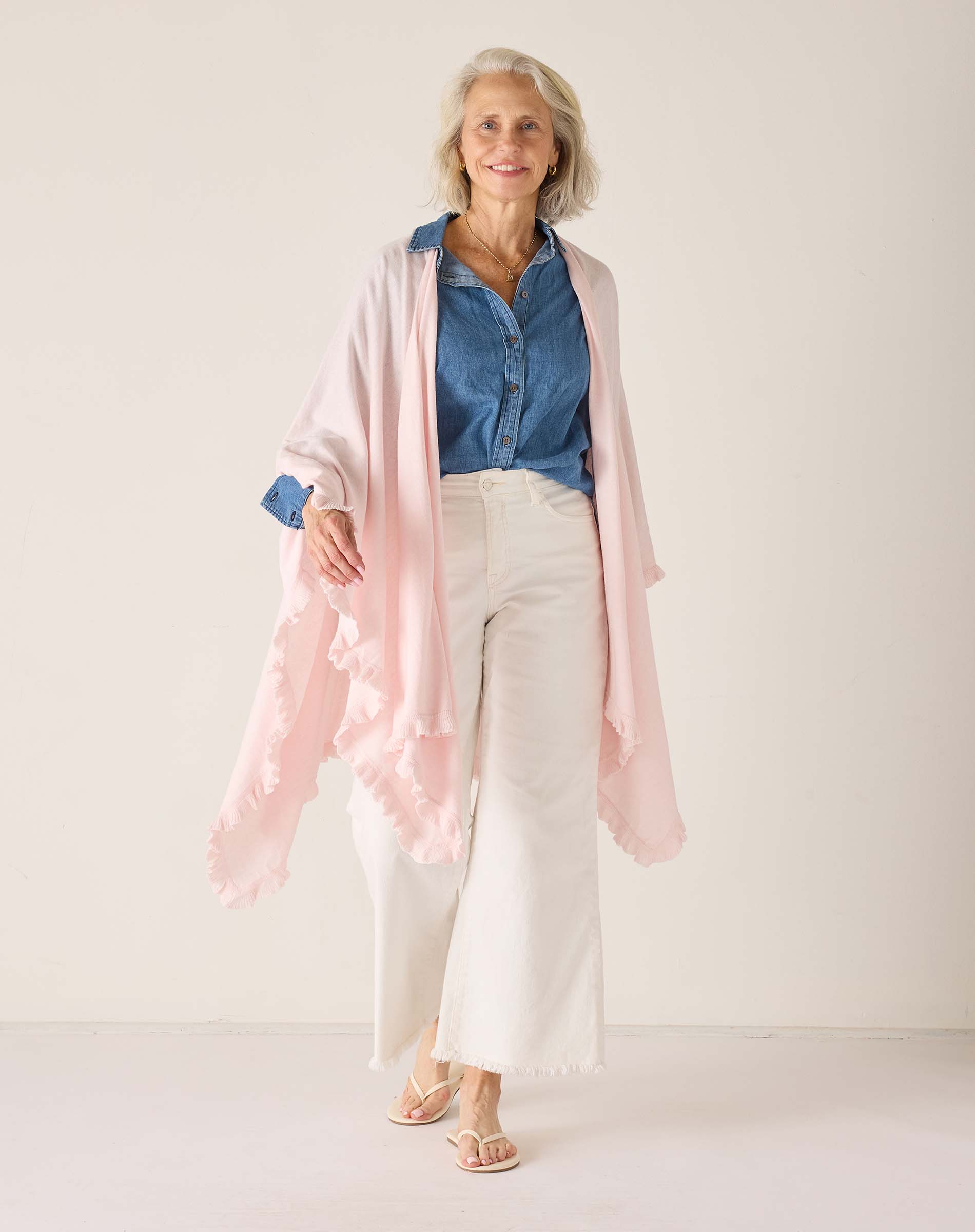 Woman wearing a blue shirt, white pants, and a pink cardigan against a white background