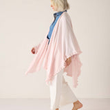 Woman wearing a light pink scarf over a blue top and white pants on a plain background