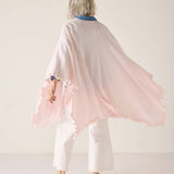 Person wearing a light pink shawl with tassels on a white background