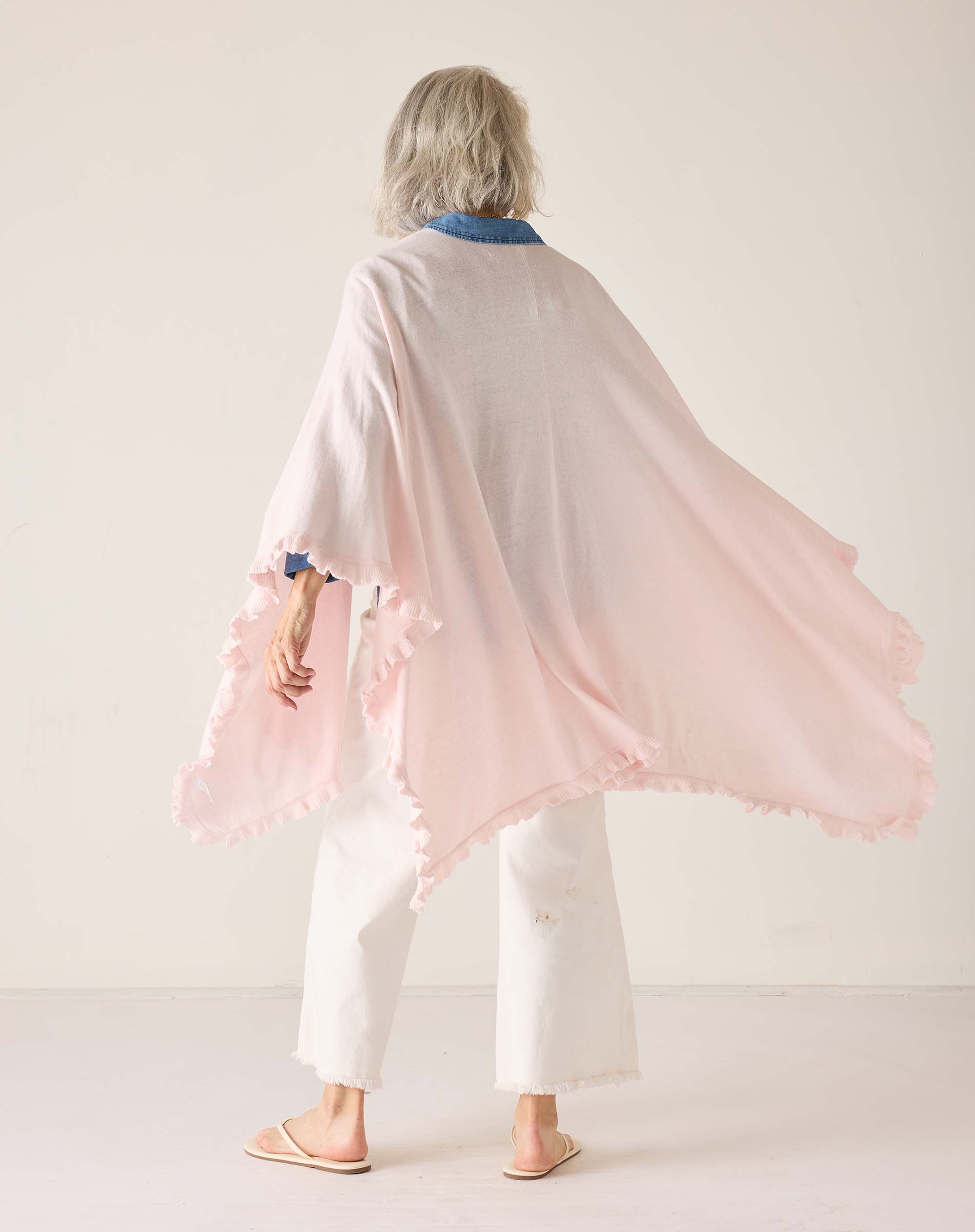 Person wearing a light pink shawl with tassels on a white background