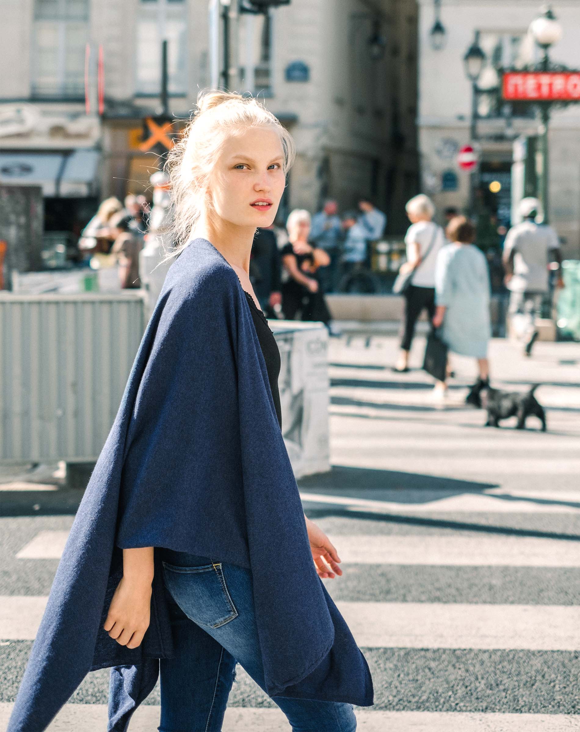 Woman in a blue coat walking on a city street with blurred background