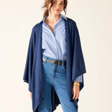 Woman wearing a blue cardigan, striped shirt, and jeans on a beige background