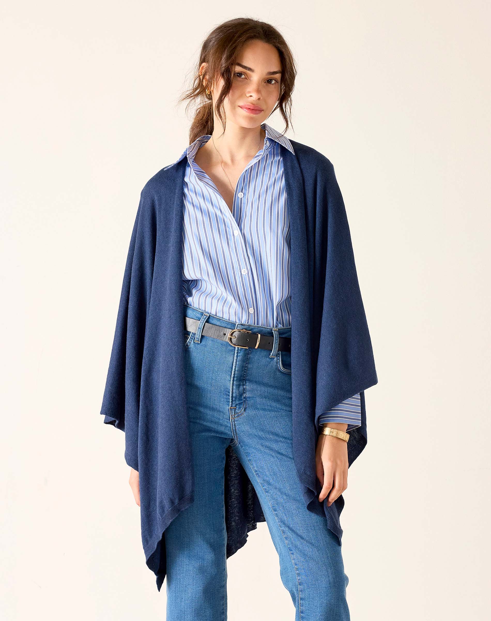 Woman wearing a blue cardigan, striped shirt, and jeans on a beige background