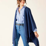 Woman wearing a navy blue poncho over a striped shirt and jeans on a white background