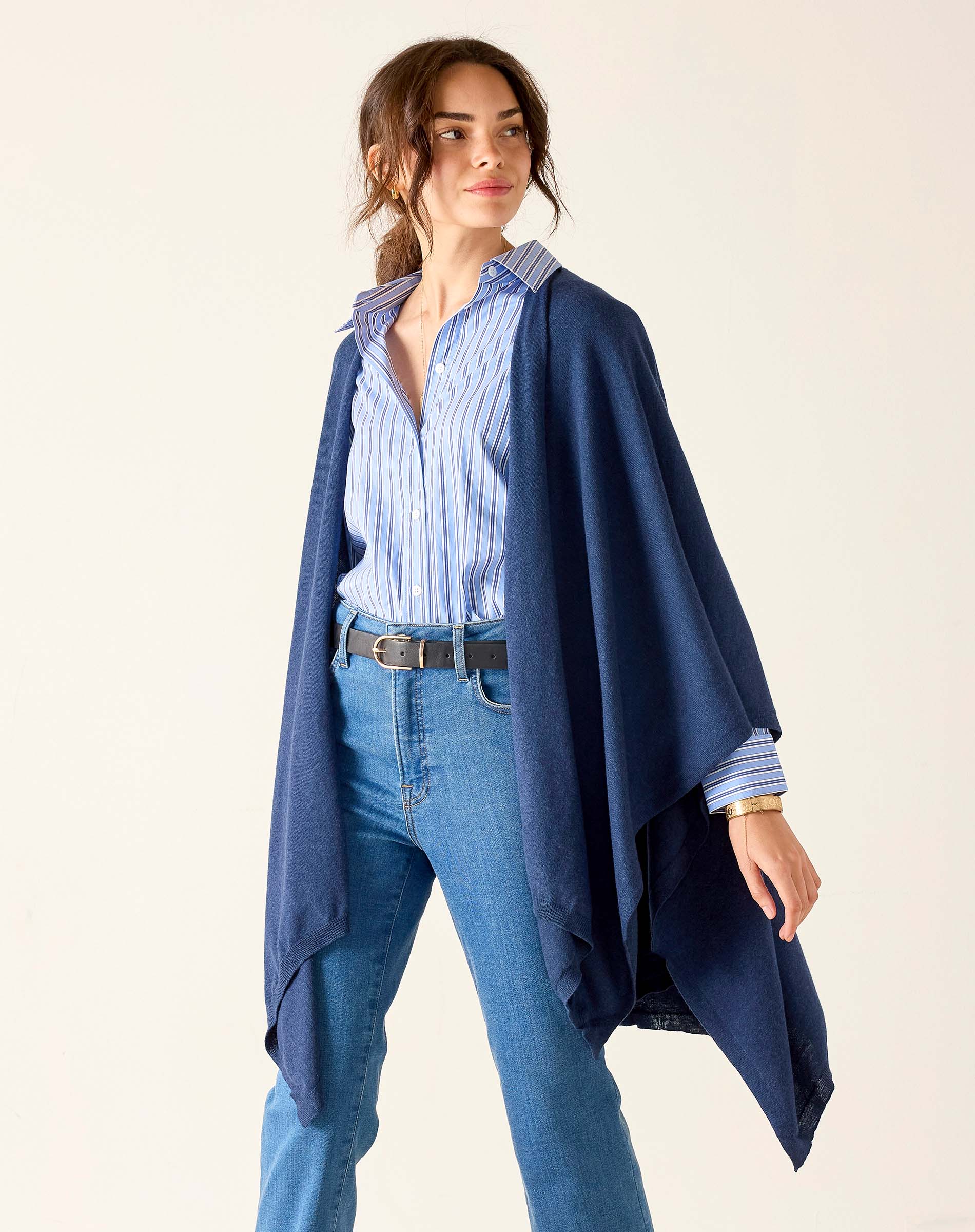 Woman wearing a navy blue poncho over a striped shirt and jeans on a white background