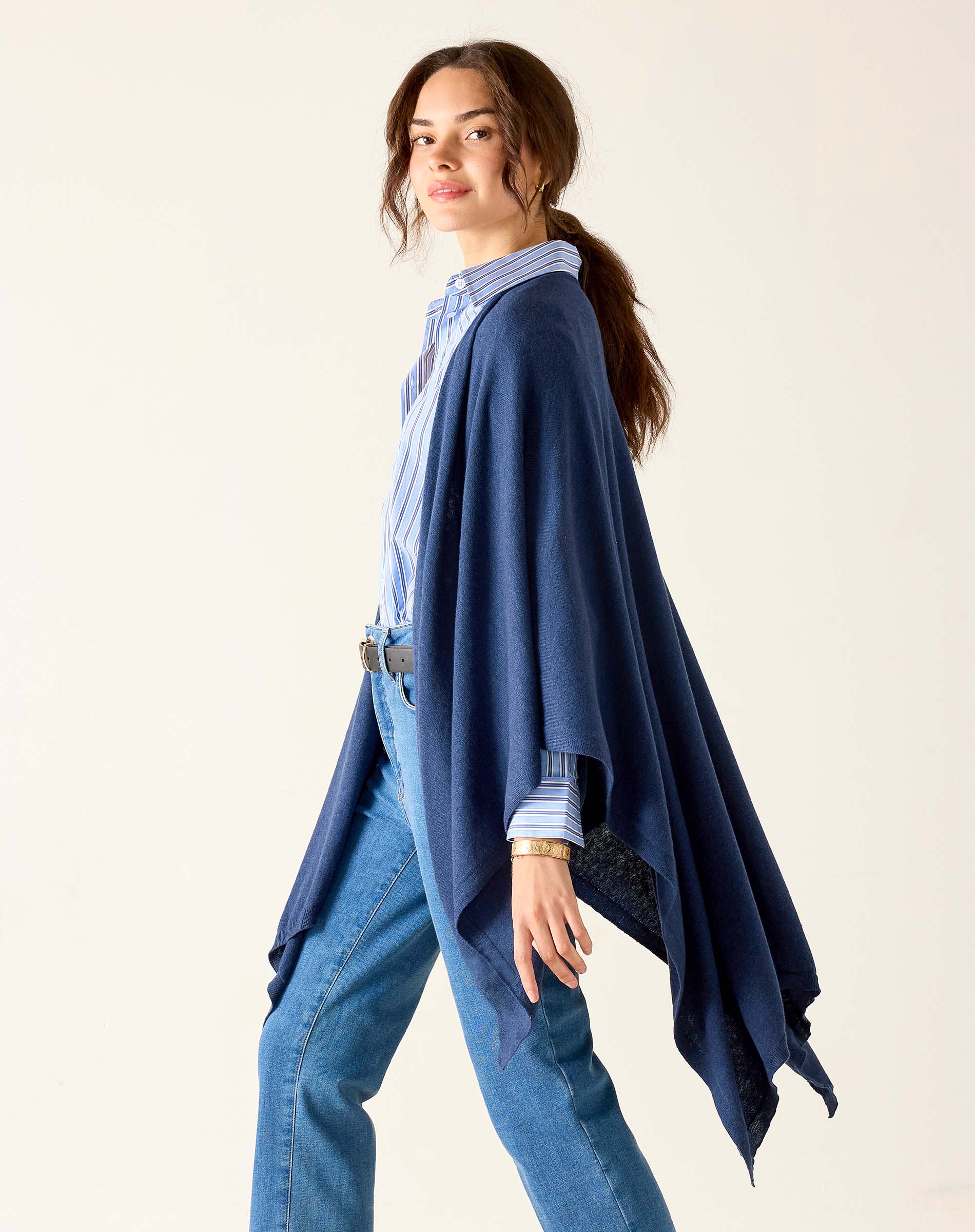 Woman wearing a blue cardigan over a patterned shirt and jeans on a plain background
