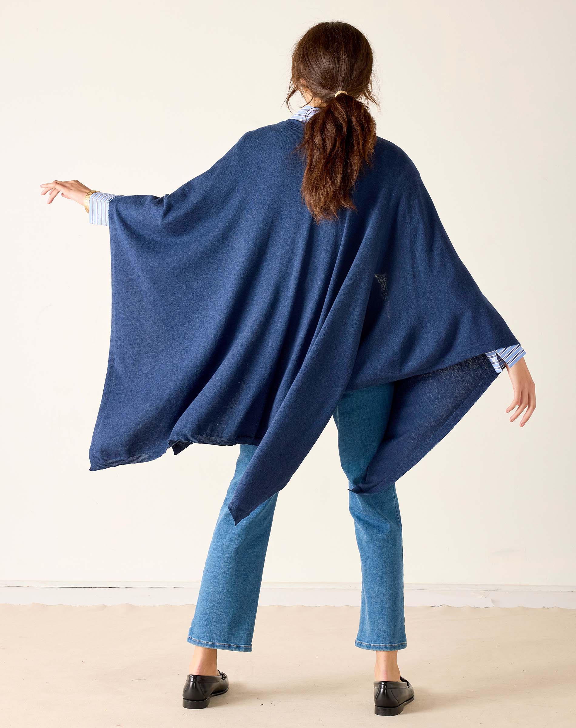Person wearing a blue poncho and jeans against a white background
