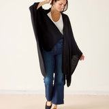 Woman wearing a black cardigan, white shirt, and blue jeans on a plain background