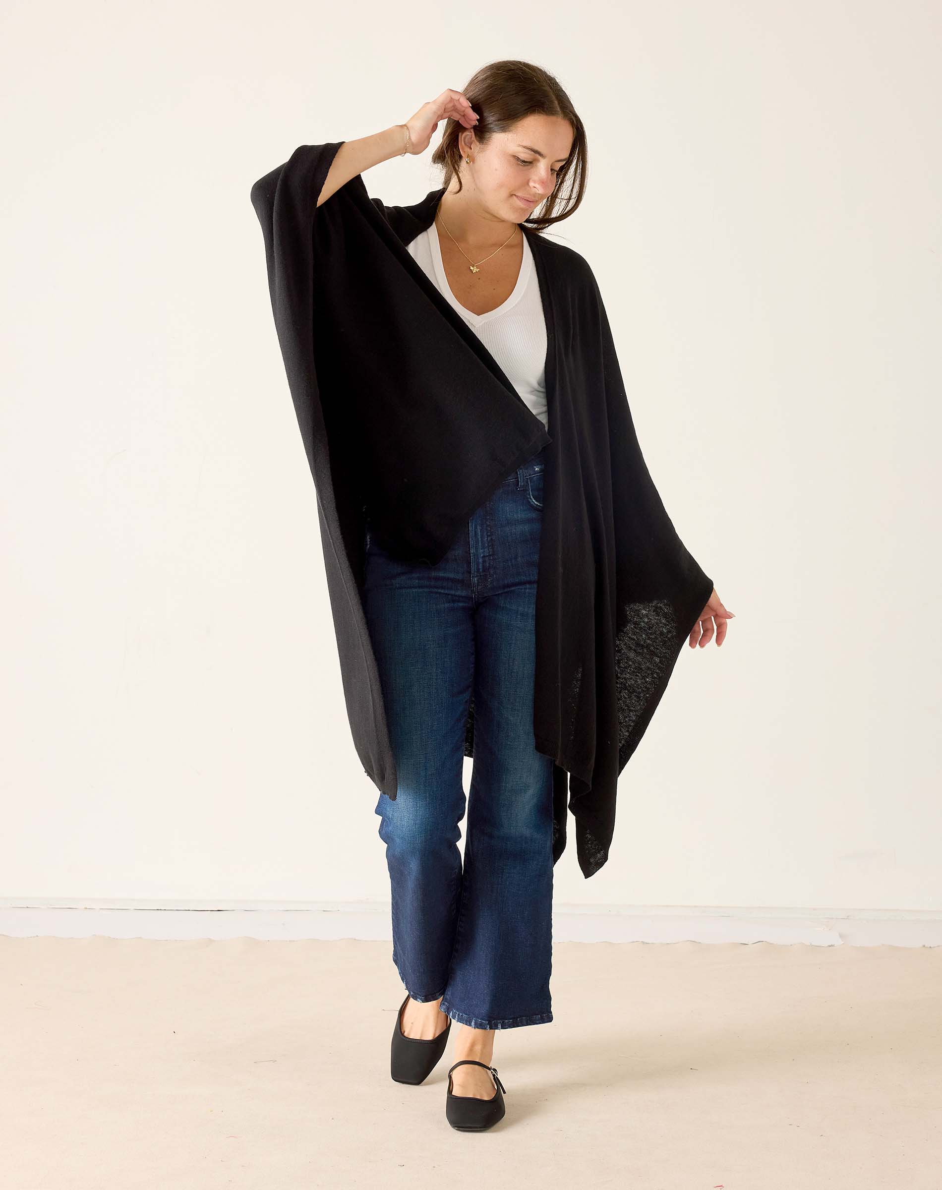 Woman wearing a black cardigan, white shirt, and blue jeans on a plain background