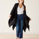 Woman wearing a black cardigan, white top, and blue jeans against a plain background