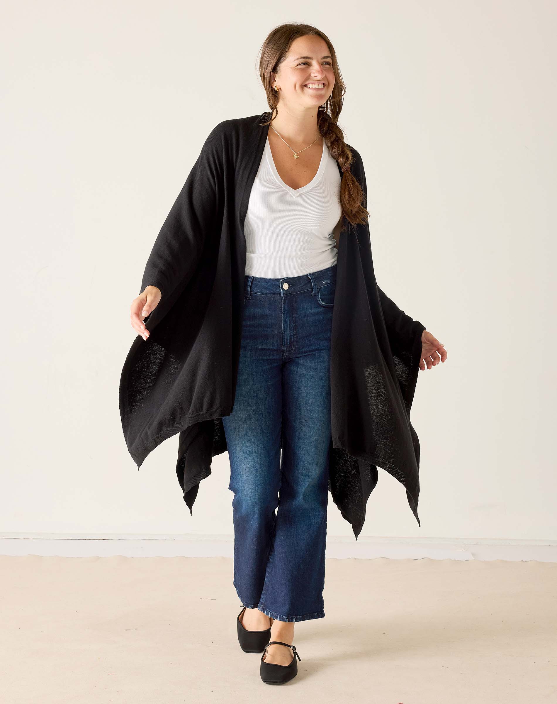 Woman wearing a black cardigan, white top, and blue jeans against a plain background