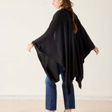 Woman wearing a black poncho over a blue outfit on a plain background