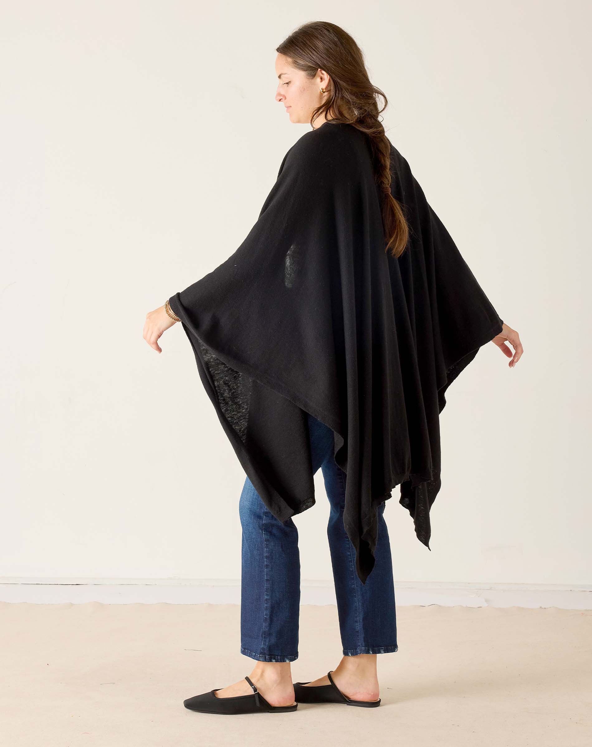 Woman wearing a black poncho over a blue outfit on a plain background