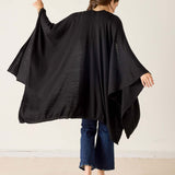 Person wearing a black poncho over a dark outfit on a plain background