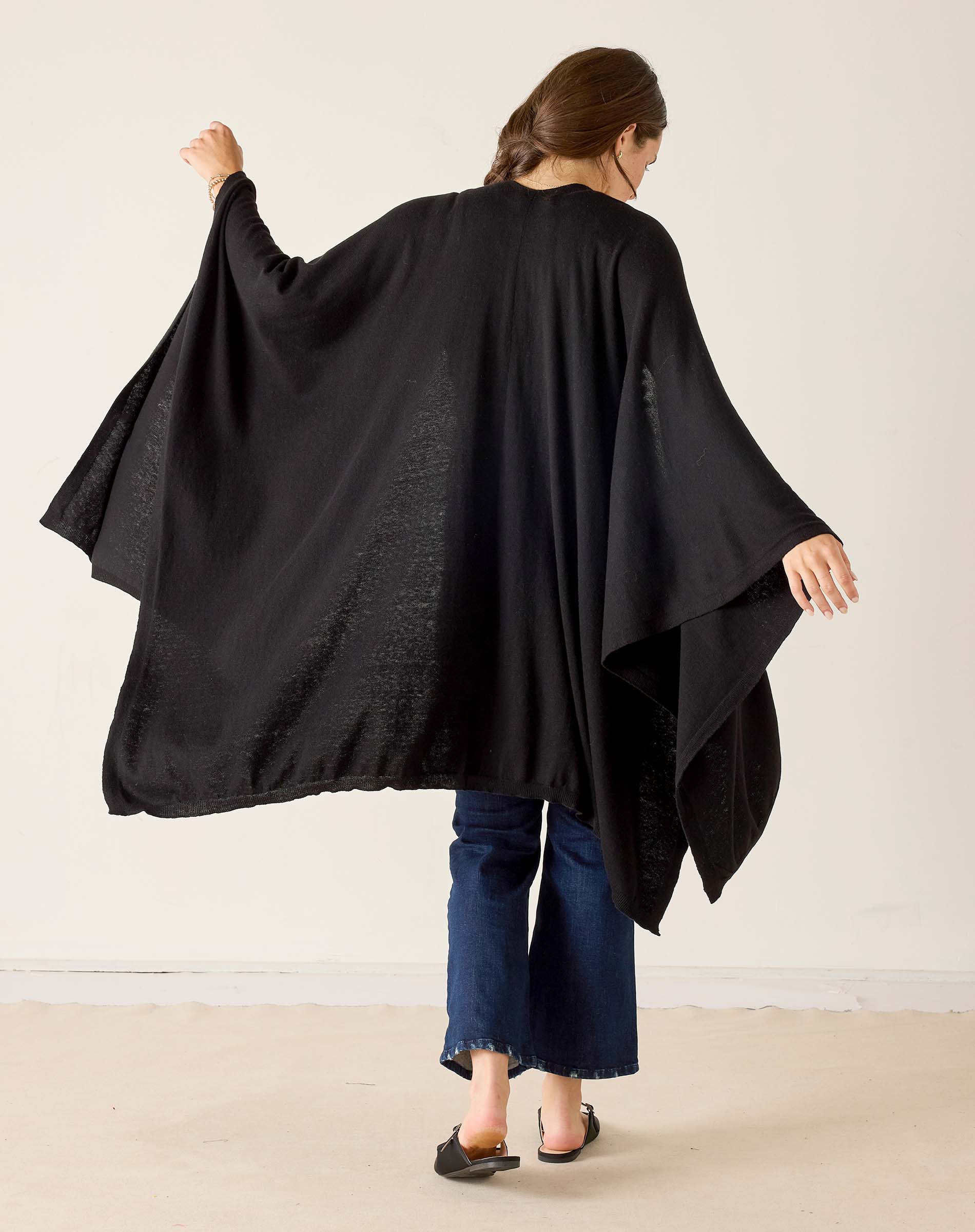 Person wearing a black poncho over a dark outfit on a plain background