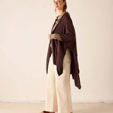 Chocolate-colored long travel wrap worn over a beige knit top and wide-leg trousers.