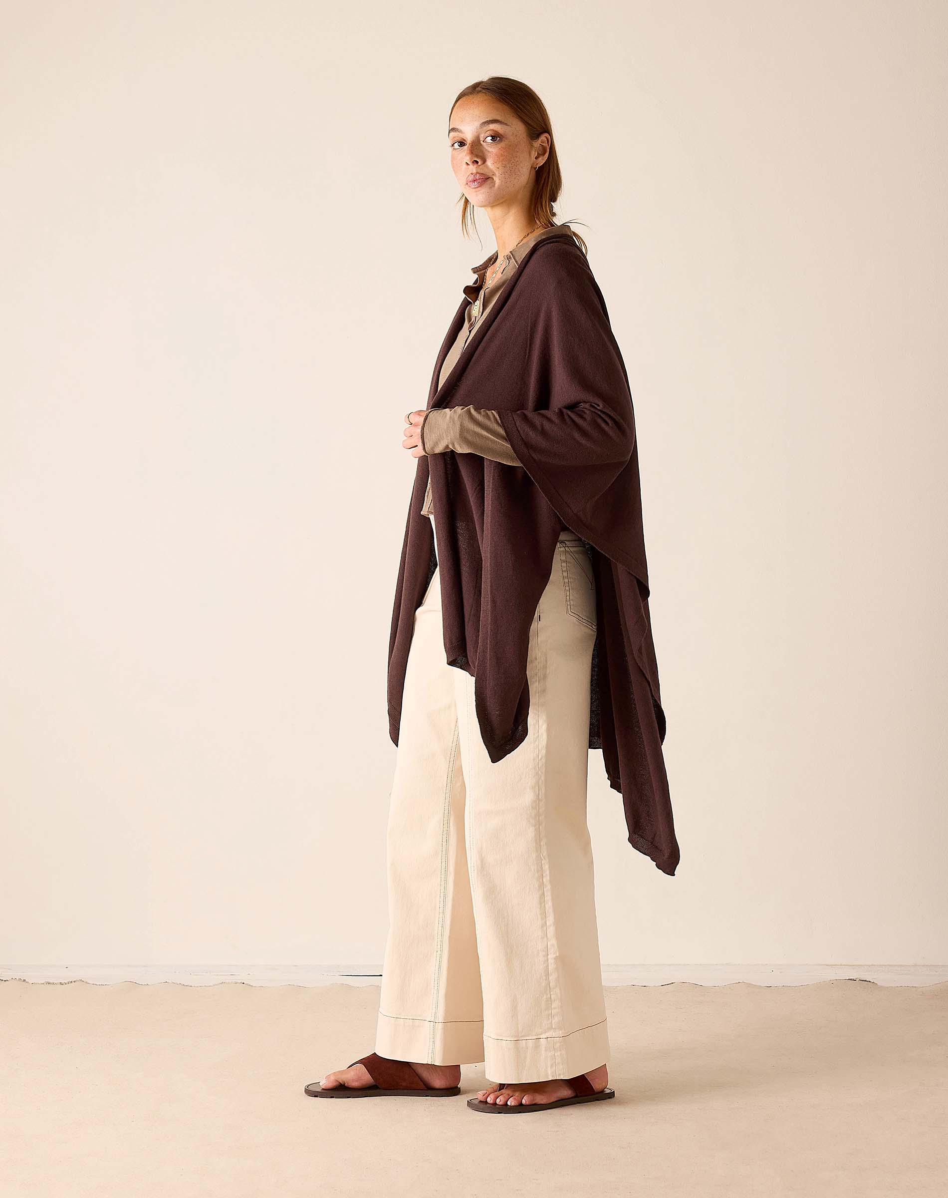 Chocolate-colored long travel wrap worn over a beige knit top and wide-leg trousers.