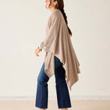 Woman wearing a beige poncho and blue jeans against a plain background