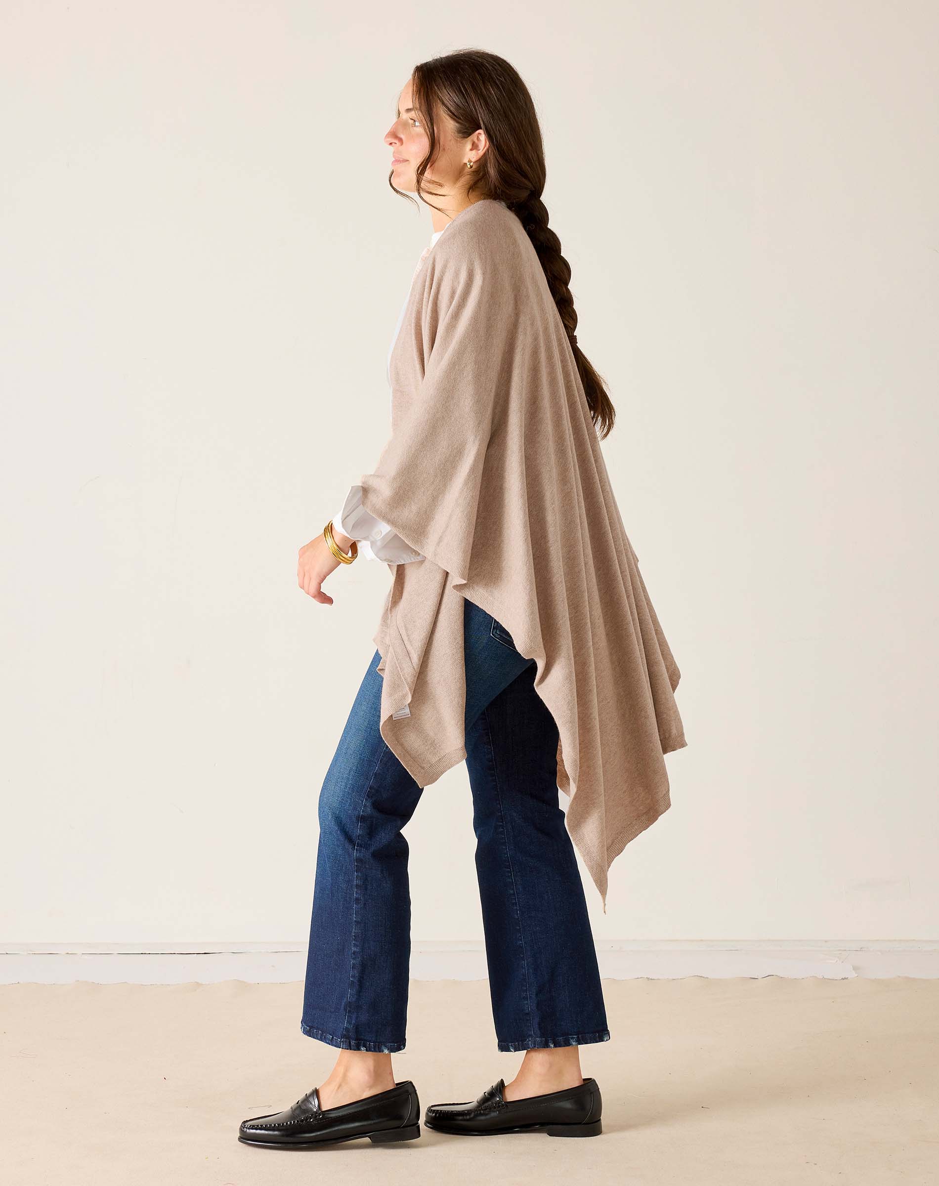 Woman wearing a beige poncho and blue jeans against a plain background