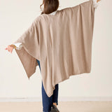Person wearing a beige poncho with arms outstretched on a plain background