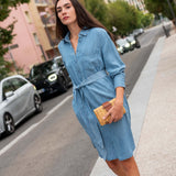 Woman in a blue dress standing on a street with cars and buildings in the background