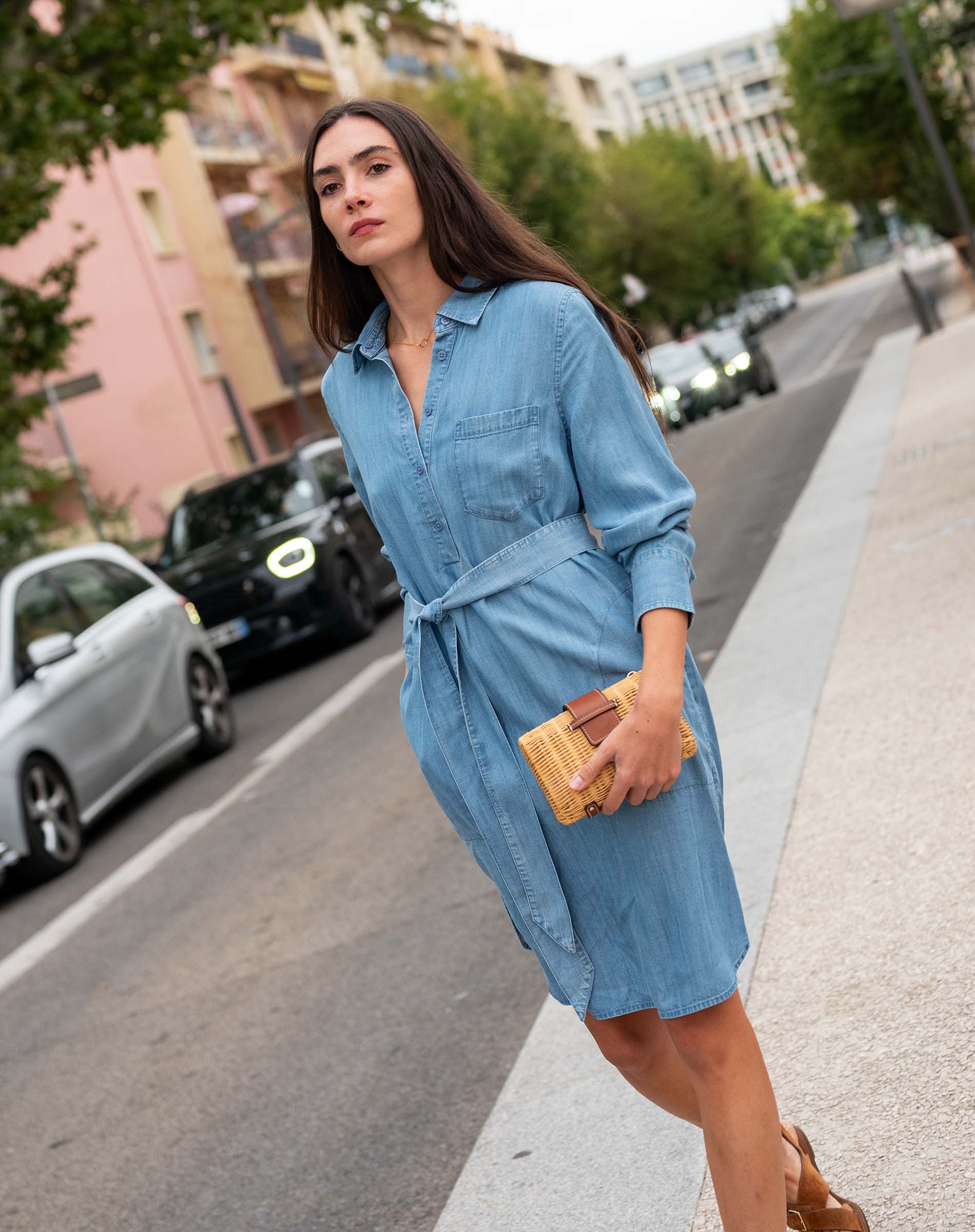Woman in a blue dress standing on a street with cars and buildings in the background