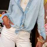 Person wearing a light blue denim shirt and white pants with accessories.
