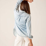 Back view of women's travel-friendly light blue button-up shirt with frayed edges and white trousers.
