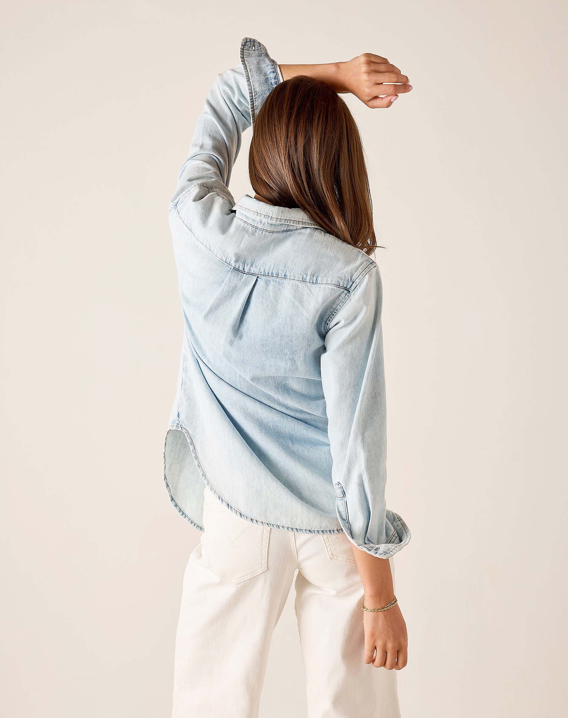 Back view of women's travel-friendly light blue button-up shirt with frayed edges and white trousers.