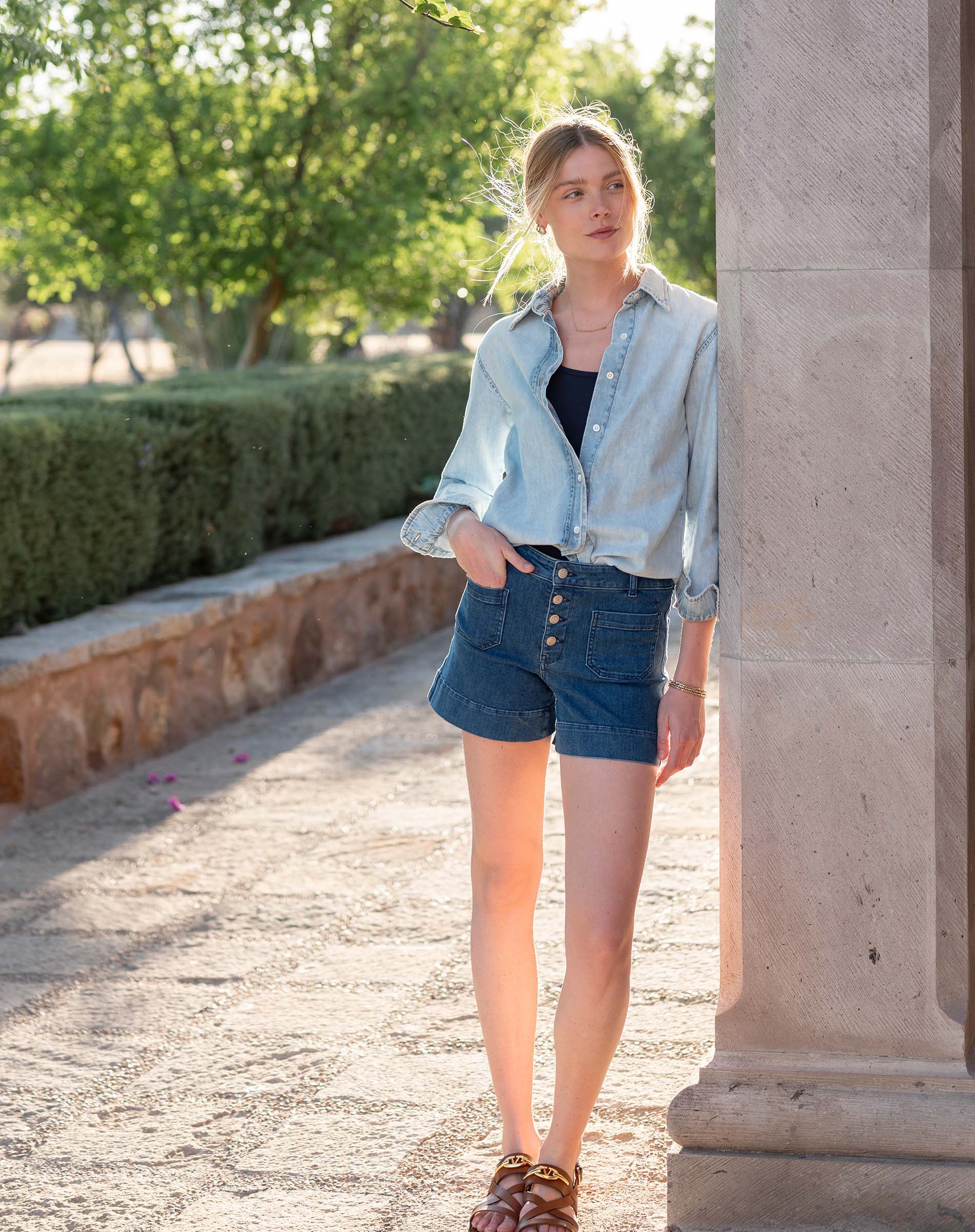 Woman in denim outfit standing outdoors near a stone column