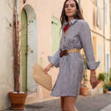 Woman in a striped dress walking down a street with buildings and plants in the background