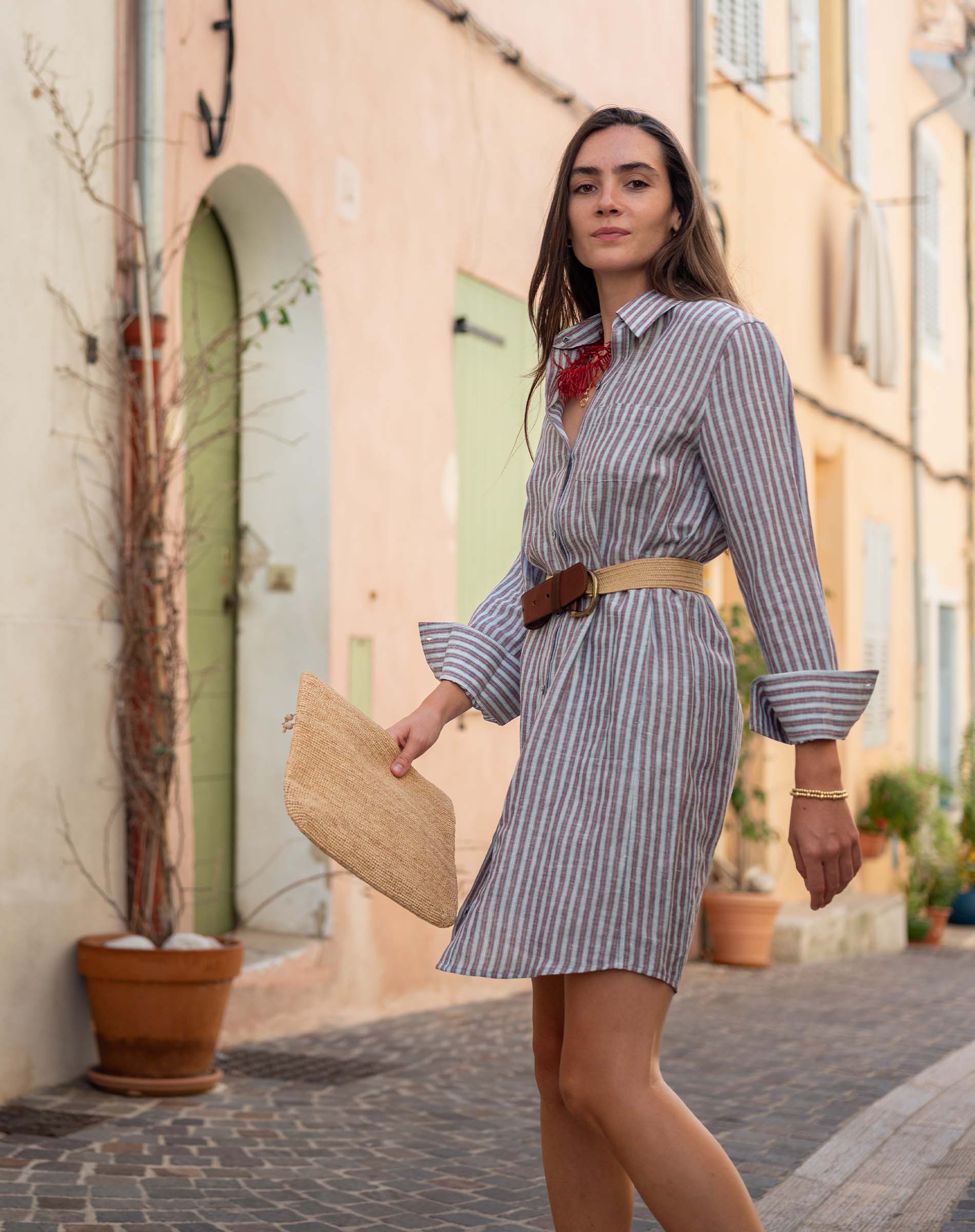 Woman in a striped dress walking down a street with buildings and plants in the background