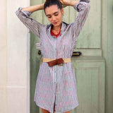 Woman wearing a striped dress with a belt in front of a green door.