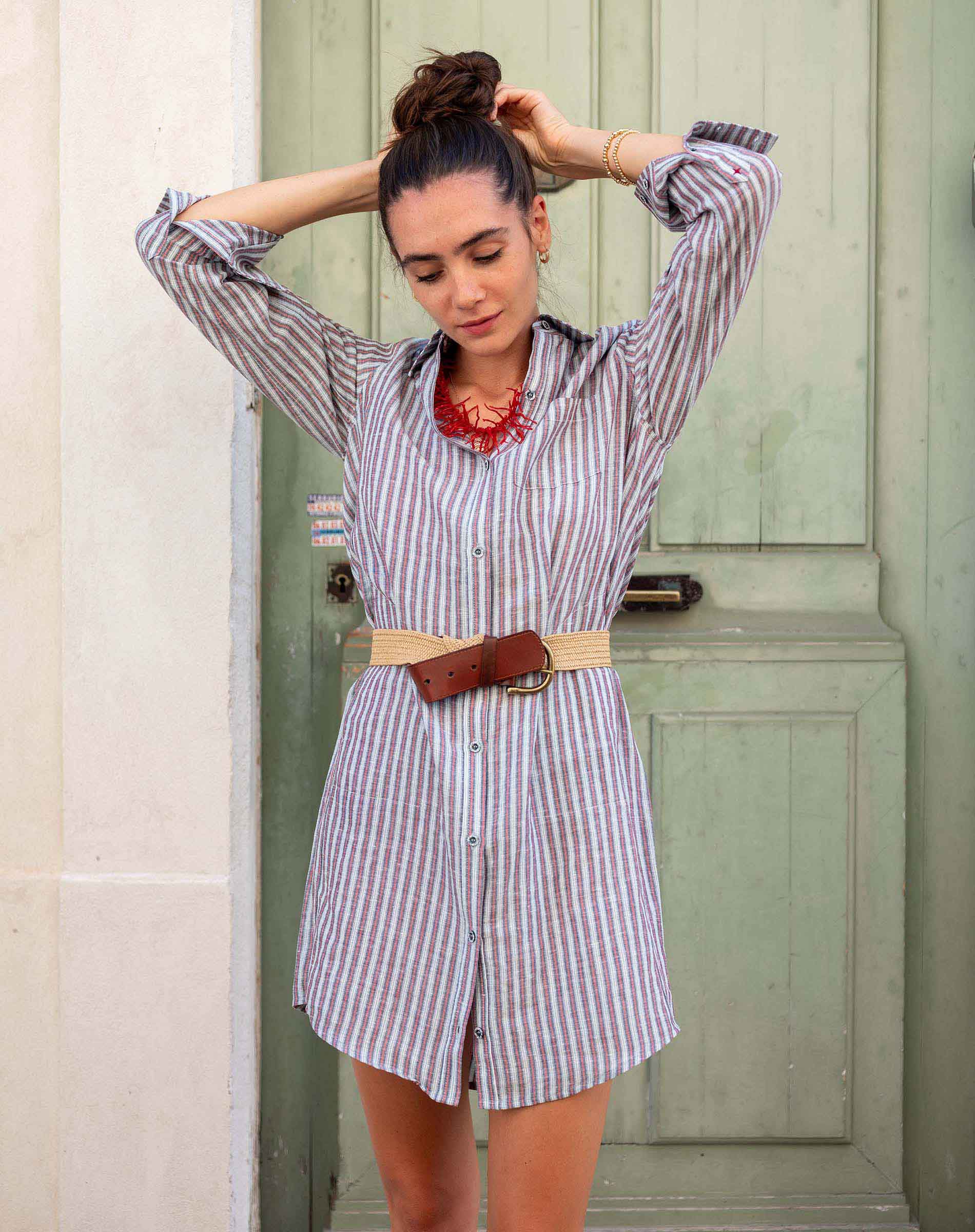Woman wearing a striped dress with a belt in front of a green door.