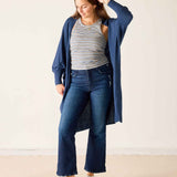 Woman wearing a blue cardigan, striped shirt, and jeans on a plain background