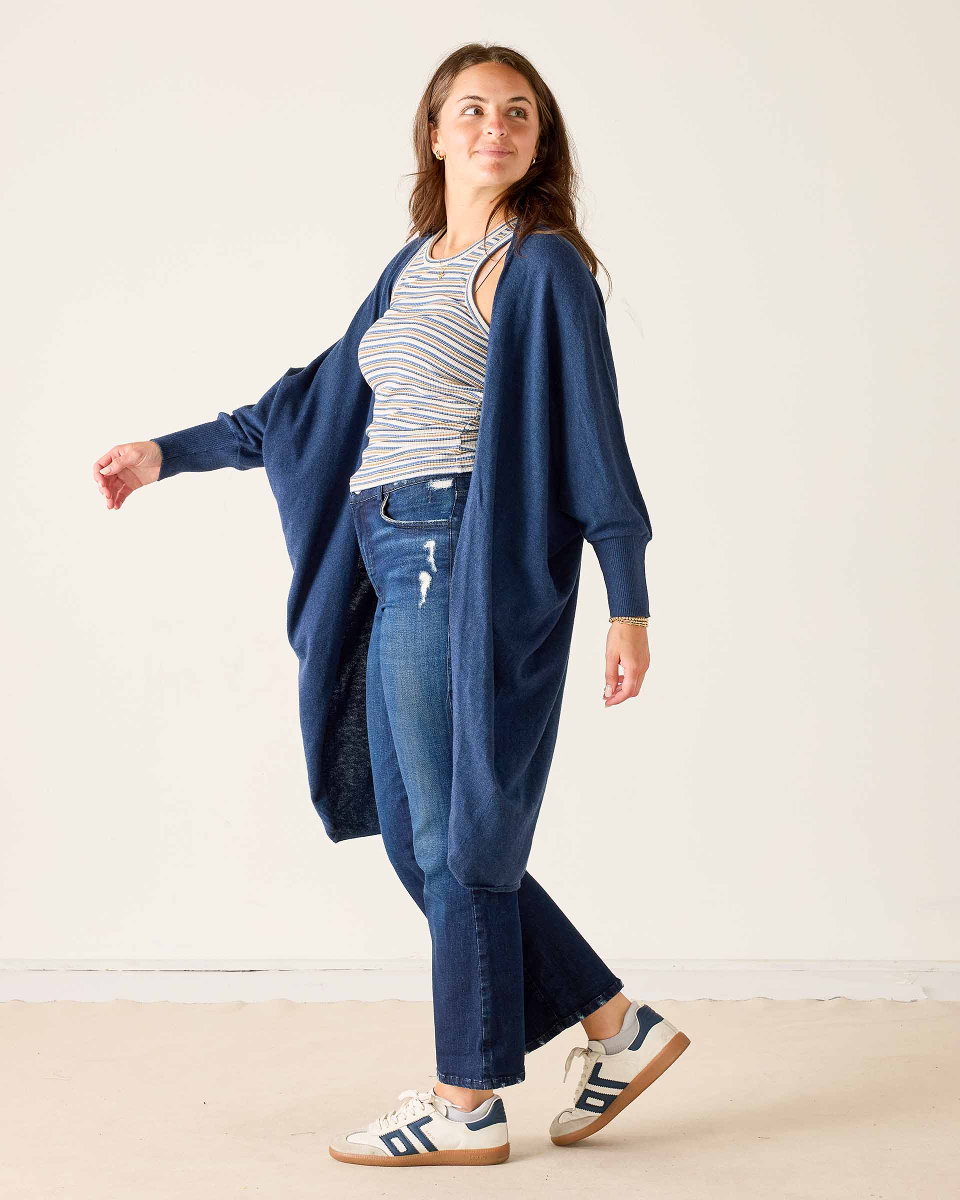 Woman wearing a blue cardigan, striped shirt, and jeans on a white background